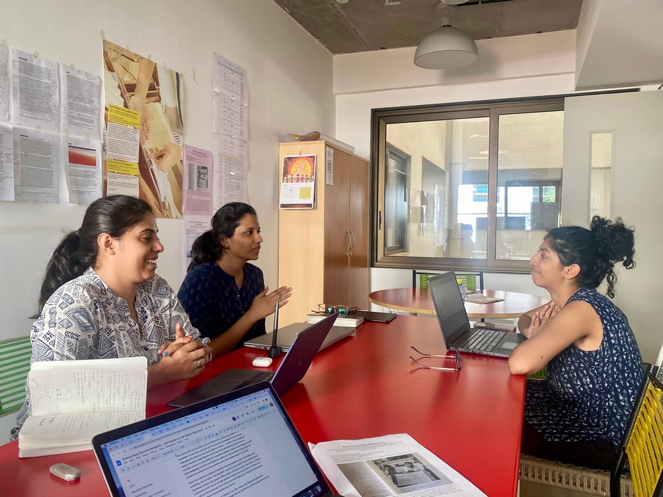 A group of lab members sitting around a red table with their laptops.