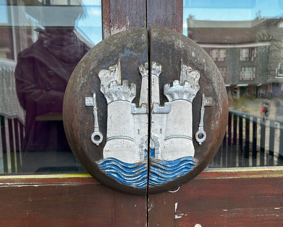 Two semi-circular door handles that form a circle. They have been carved with the town's coat of arms. The wood is looking worn and tinged with green in parts.