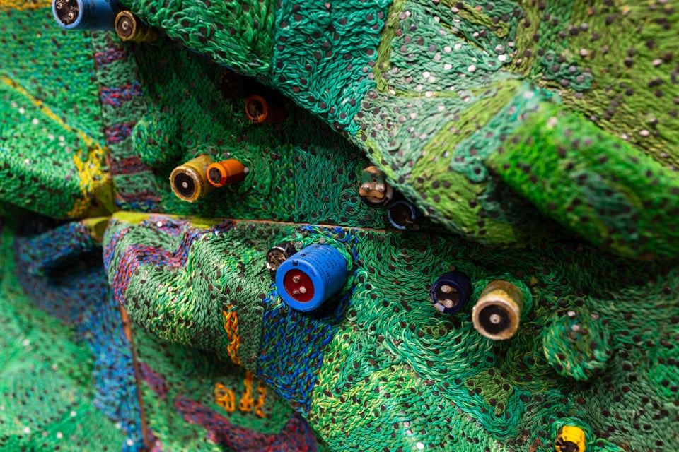 A closeup of the above painting. It is a dense green undulating surface that seems like plastic or textile, with colorful and cylindrical capacitors pointing out it