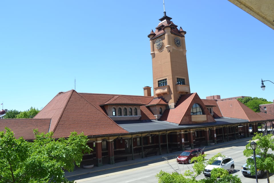 A large building made from orange brick and red tile with a very tall clock tower in the center.