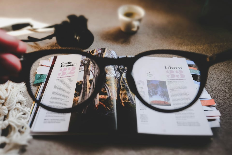 A close-up of glasses held over an open magazine.  Photo by Ewan Robertson on Unsplash