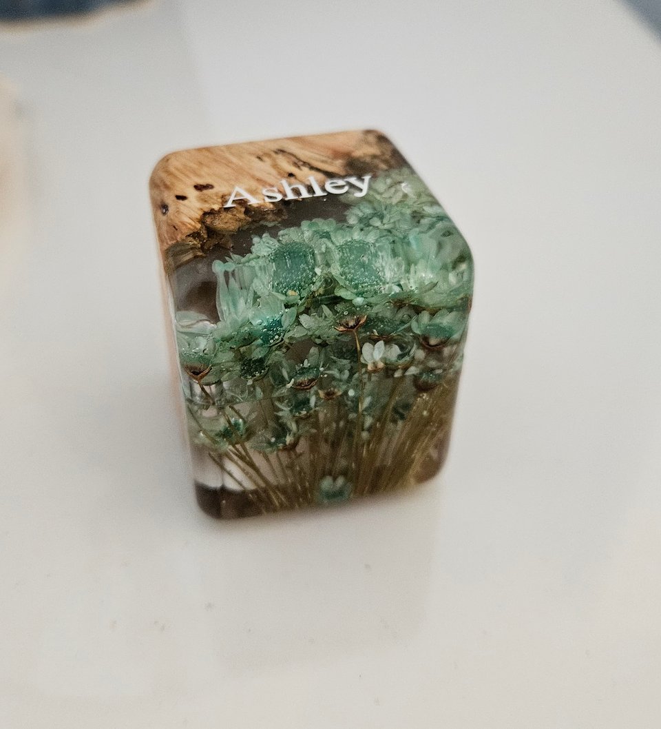 A ring box made of a mix of bamboo wood and tiny teal flowers encased in a plastic material. The name Ashley was enscribed on the top.