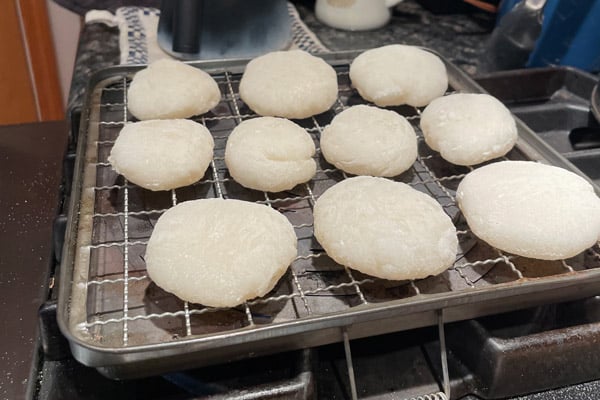 Photo of ten round white mochi pieces on a grill set on a stovetop