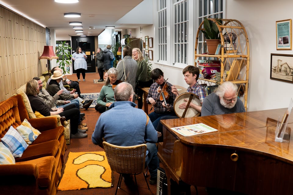 Candid shot of NCC lounge with irish musicans in the foreground playing music while audience members amble about in the background