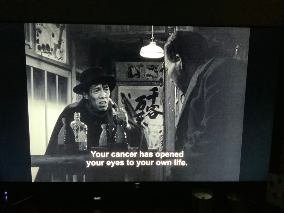 Still of movie Ikiru, showing two men in a bar; subtitles read, "Your cancer has opened your eyes to your own life."