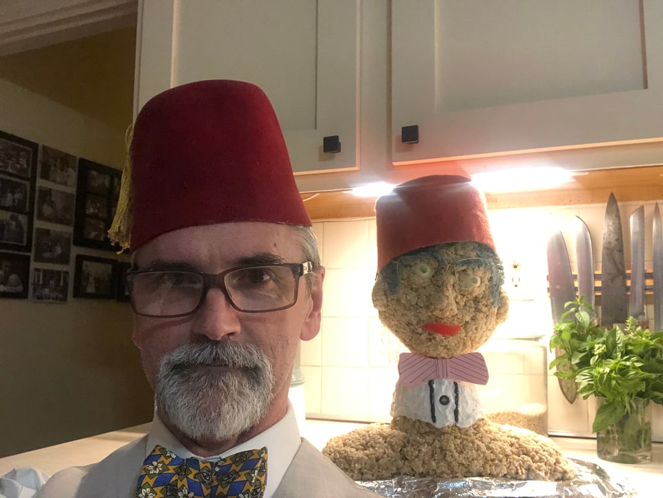 Photograph of Ed posing in front of a Rice Krispie treat cake in the shape of his head and shoulders. Both are wearing red fezes, glasses, and bow ties.