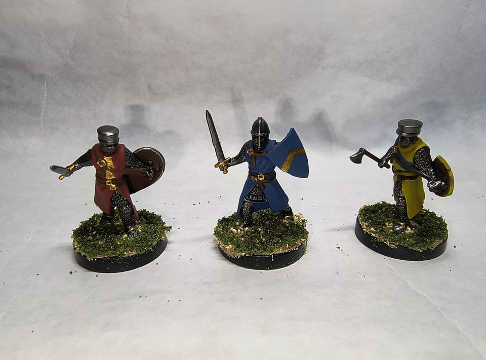 Three knights, one with a red surcoat with a gold pale, one with a blue surcoat with a gold chevron, and one with a yellow surcoat with a blue bend