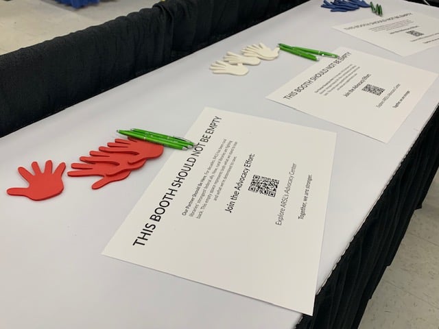 Image from the Association of Rural and Small Libraries. The convention center exhibit hall had an empty booth set up for the IMLS. The image shows some hands people can write on to show solidarity with the IMLS.