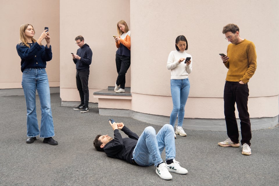 A team photo of all our six members, standing in front of a building wall, all looking at their phones, one person lying on the floor