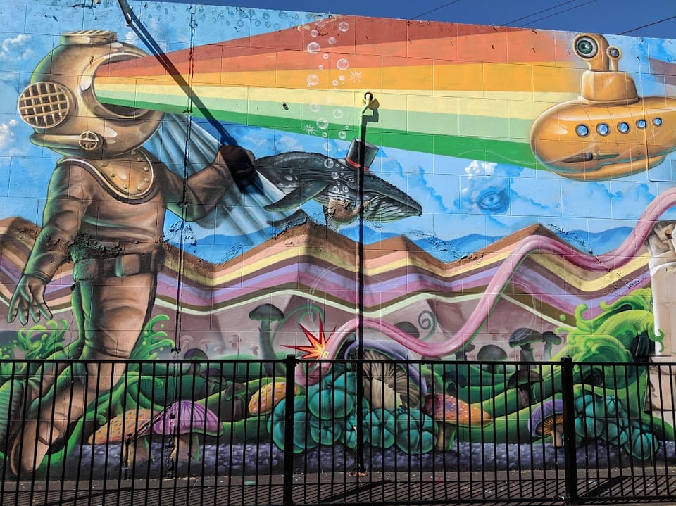 A person in a diving costume shoots a rainbow out of their face. There's a whale in a top hat and a fancy submersible.