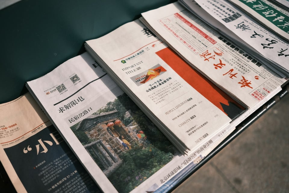 A man in sunglasses, seated, reads a nespaper. Photo by Zahra Amiri on Unsplash.
