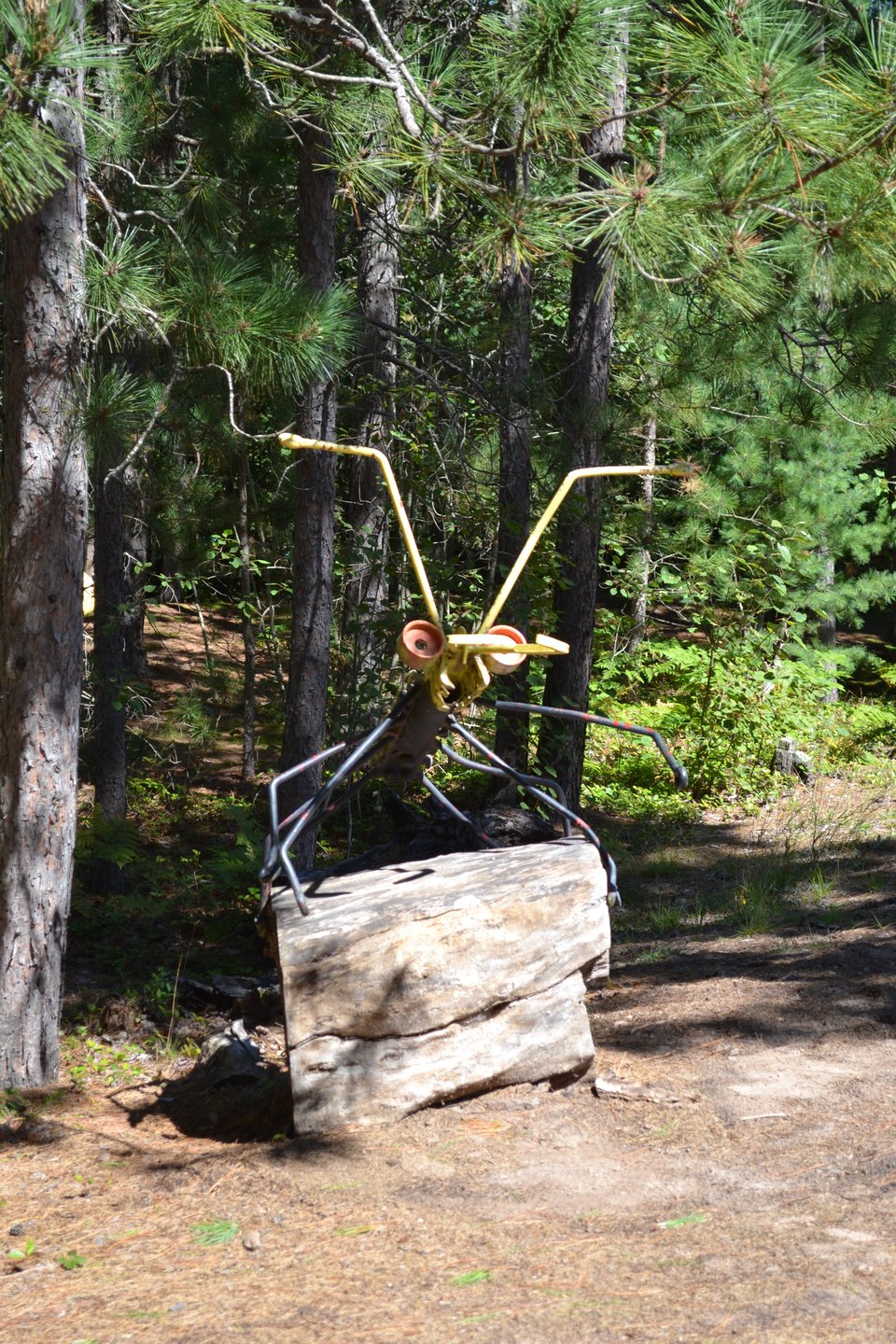A sculpture of a very large ant made out of metal, standing partly upright with its legs on a stack of logs.