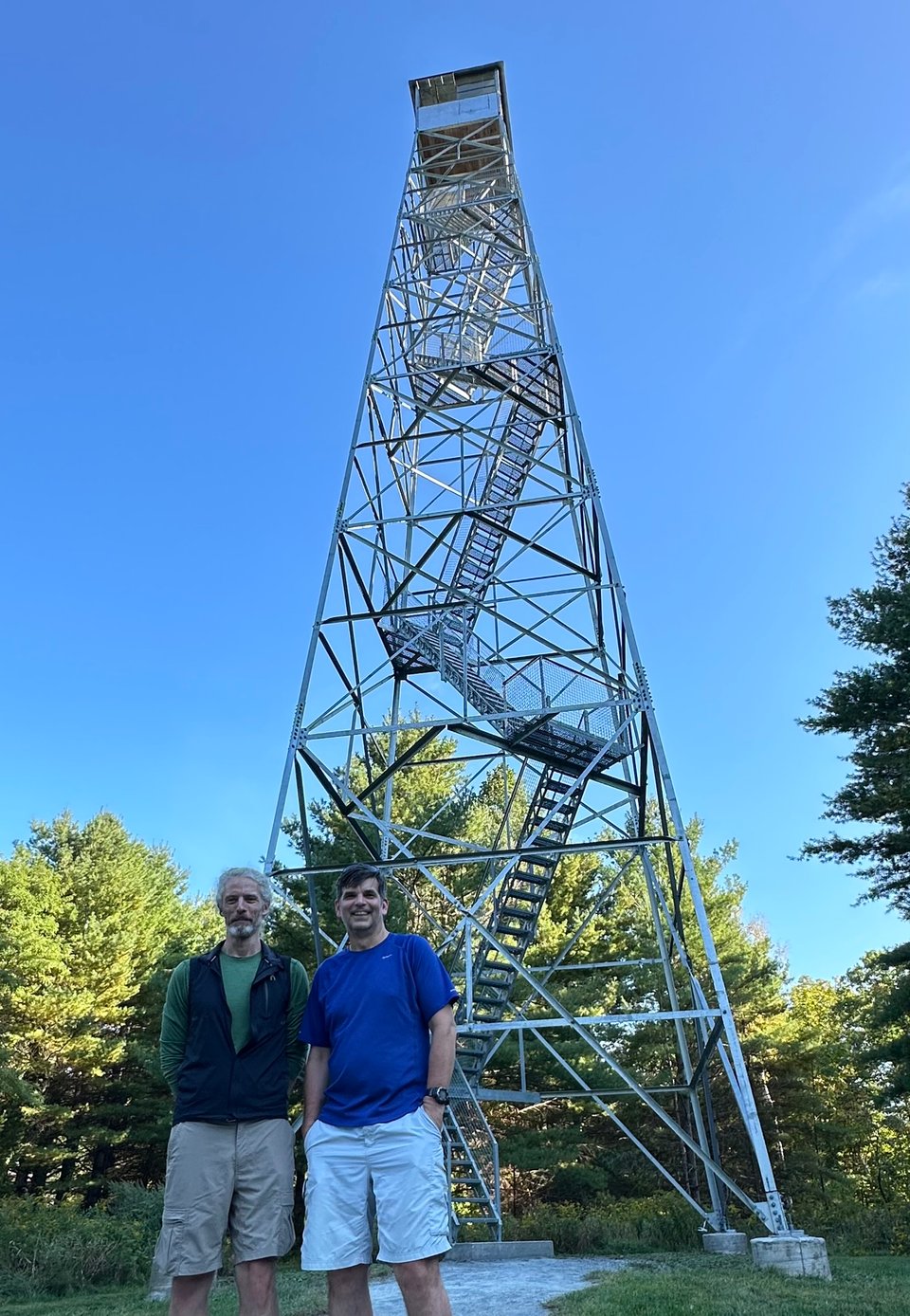 Photo of 2 white men standing in front of a tall metal fire tower