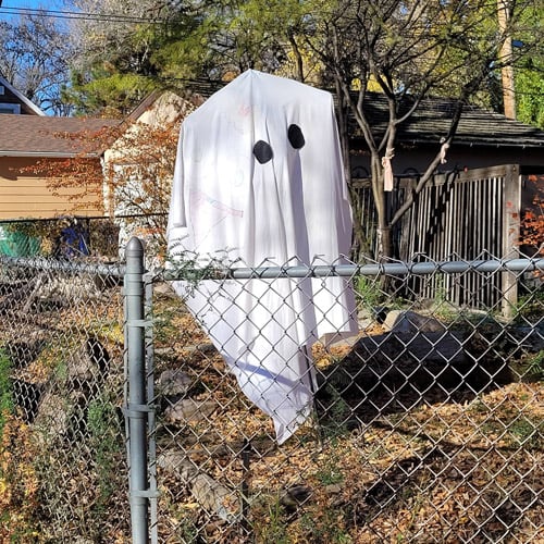 A makeshift ghost decoration made from a bedsheet with what looks like felt eyes. The sheet is attached to both a coat hanger at the top, hanging from a wire, and then all this is also attached to a stake in the ground. You can't really make it out in the photo, but the sheet also has several cartoon creatures drawn on it.