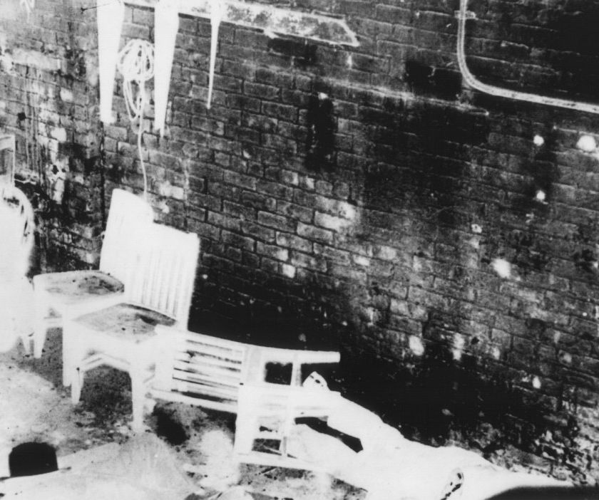 Black and white photograph of the wall in the garage. There are chairs that are infront of the wall and some have fallen to the floor.