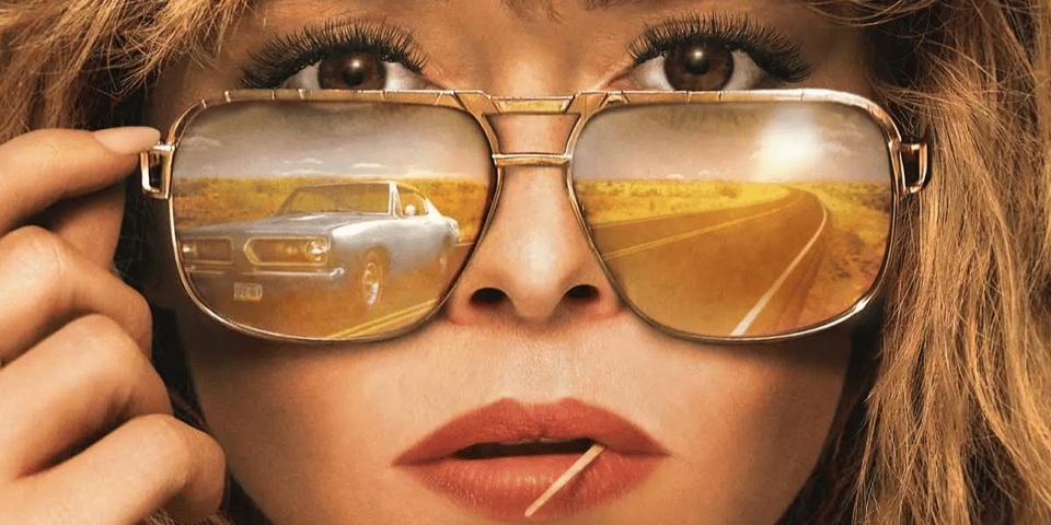 Natasha Lyonne looking awesome, wearing aviator sunglasses with a car in the reflection.