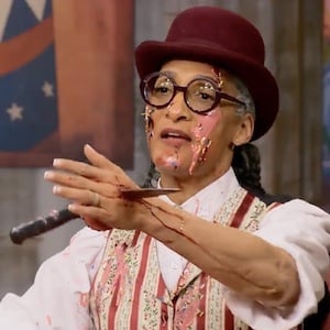 Carla Hall in a Halloween costume with a bowler hat and a fake knife through her hand