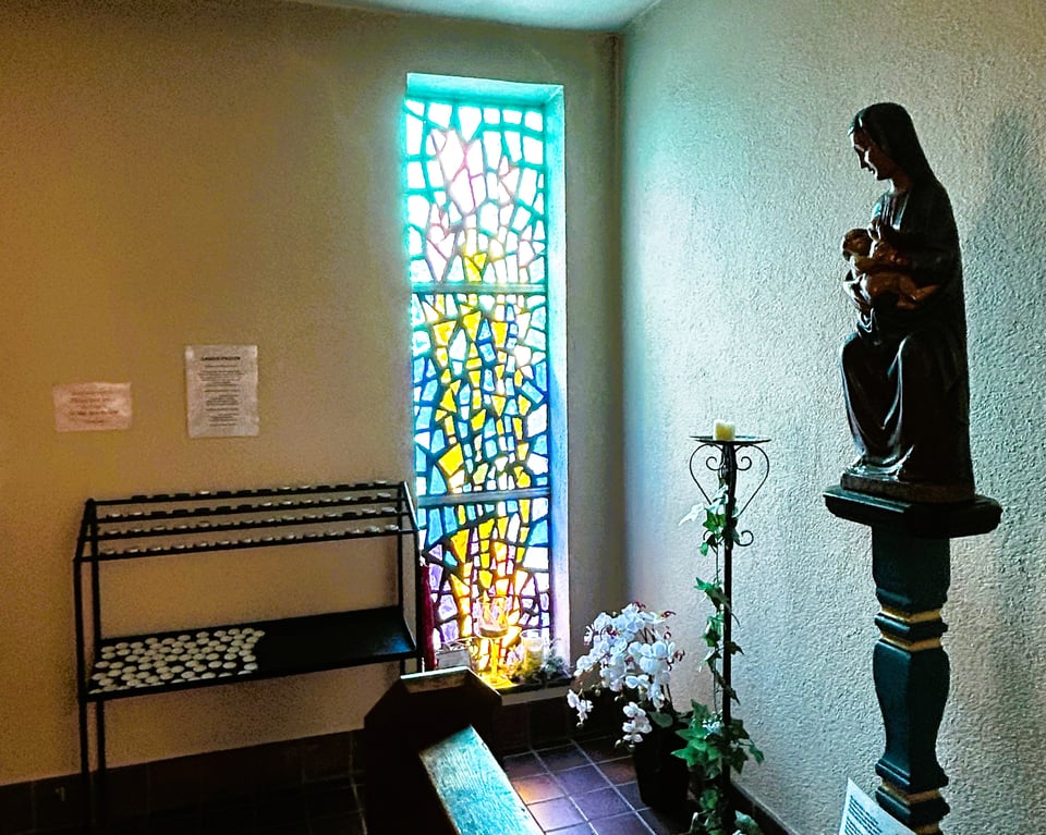 A window made up of blue, white and purple glass with a cascade of yellow through the centre. It's light reflects on a small statue of the Madonna and child.