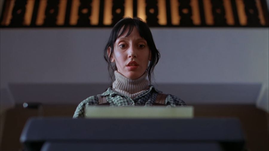 Shelly Duvall looking down at a piece of paper in Jack’s typewriter, a stunned look on her face.