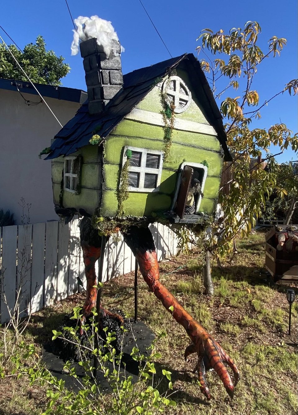 A DIY build of a little green cottage on top of chicken legs. It's standing in someone's yard
