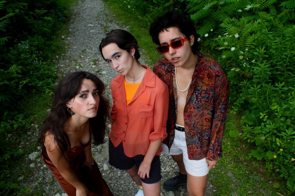Three people stand on a gravel path in the woods, looking at the camera.
