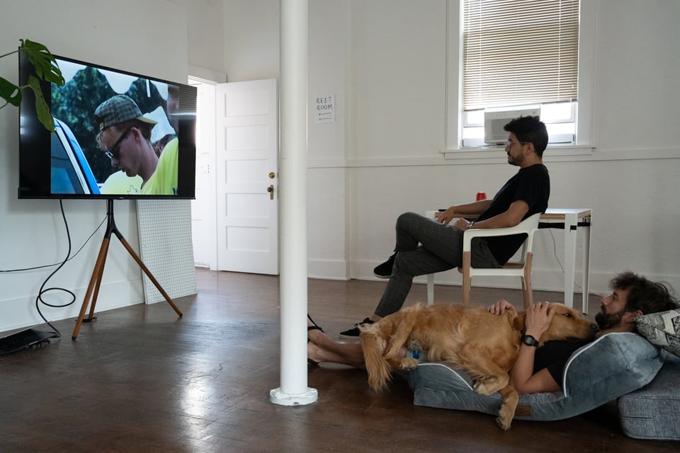 Two people watching a TV with a dog on one of them.