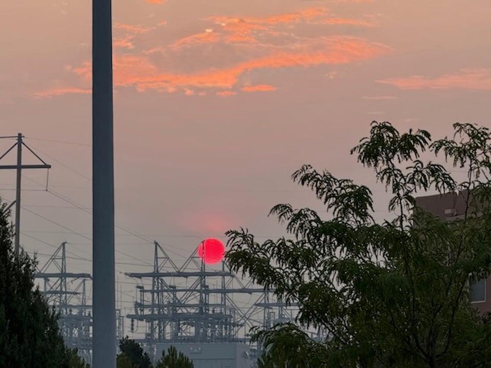 sunrise over power plant. sun is deep red in color because of wildfire smoke.