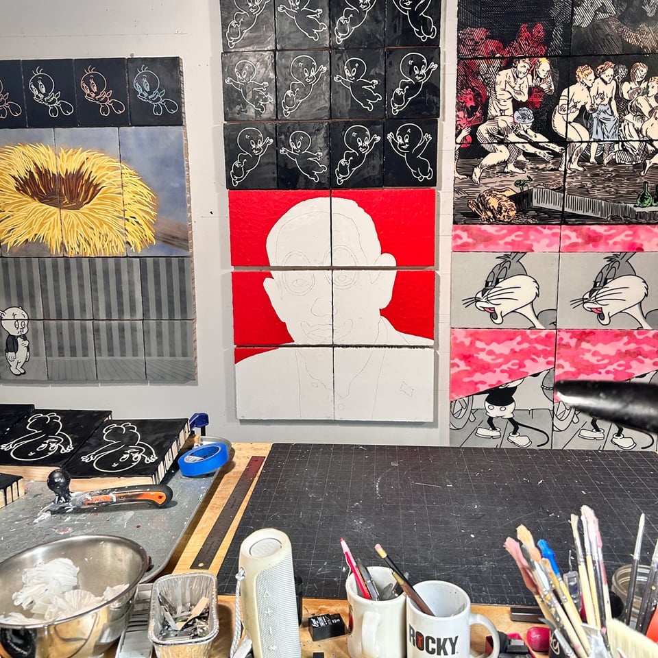 messy studio with various shitty paintings hanging on the wall.