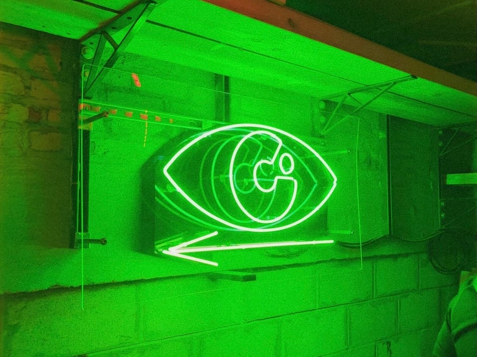 A green neon sign of an eyeball with a "C" in the middle for the pupil