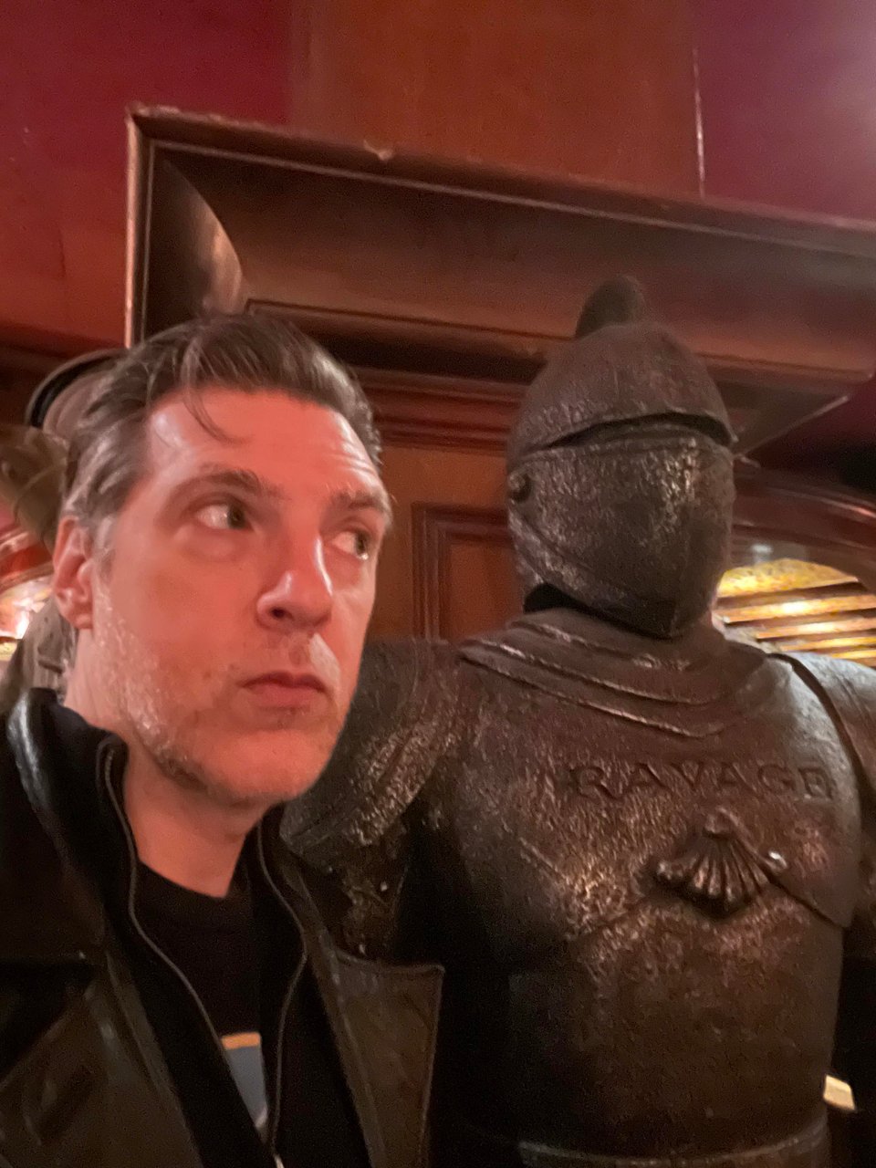A man looks behind and sees a lurking suit of armor in a red bar