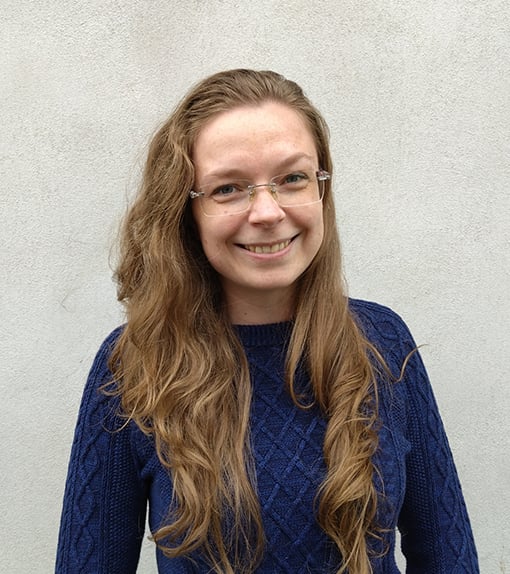 A picture of a white woman with blonde hair in a blue sweater. She is wearing glasses and smiling happily in the camera.