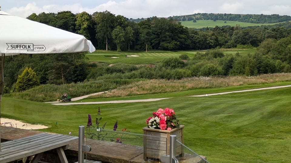 A view of Cavendish Golf Club, Buxton, in summer from the clubhouse veranda looking across the 18th fairway with the 7th hole and Derbyshire hills in the background.