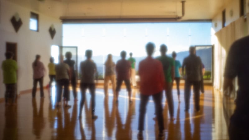 A soft-focus pinhole camera image of a group of people doing the standing meditation in horse stance, with a blue sky and mountain view in the background