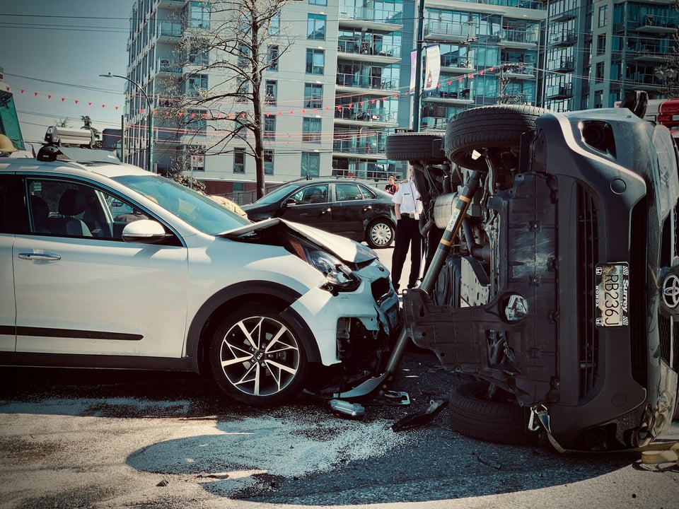 One car that has crashed into the other.  The second car is on its side.  Photo by Anthony Maw on Unsplash.