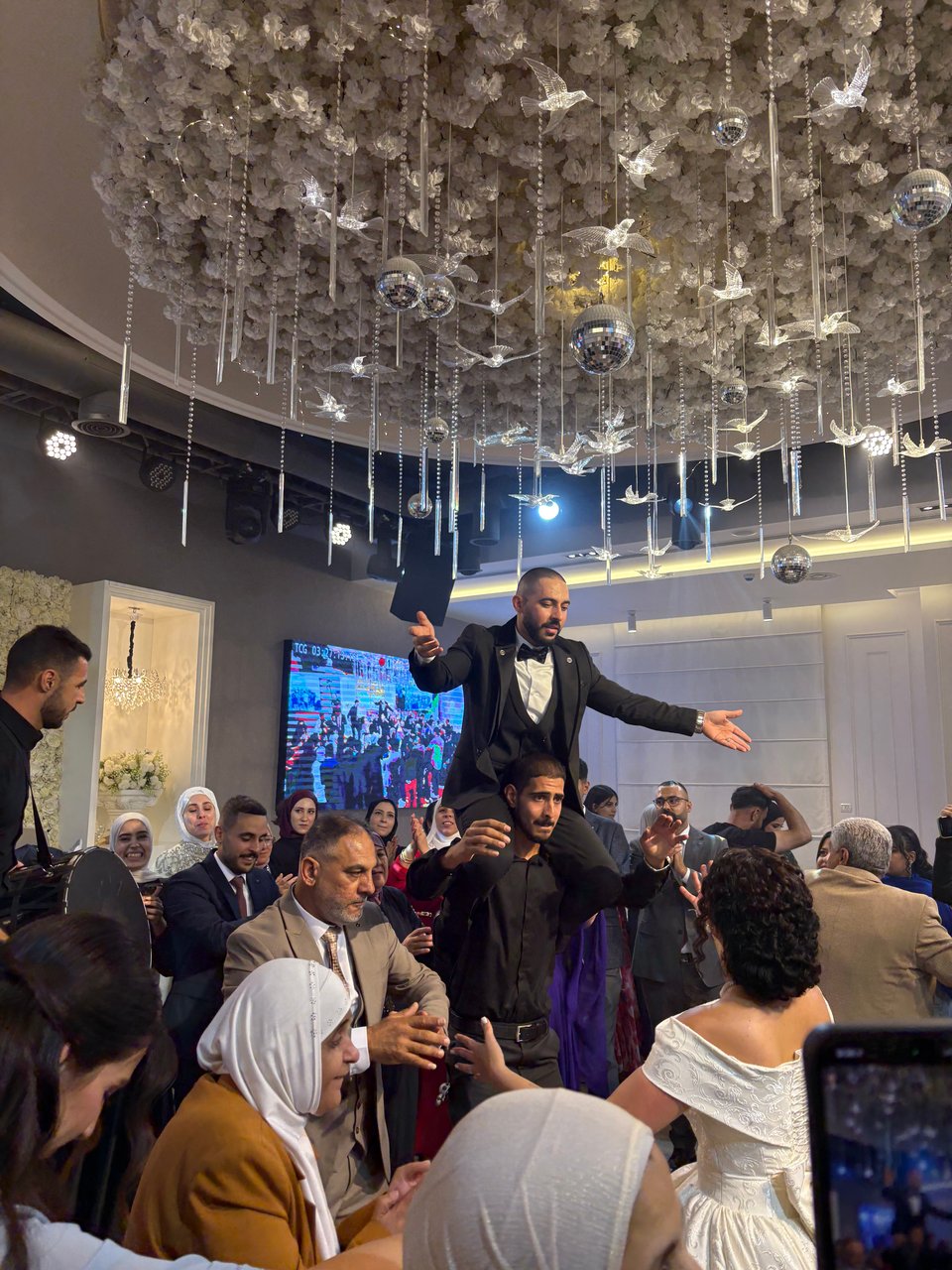 A group of people dancing, with the groom, in a tuxedo, lifted on the shoulders of a man