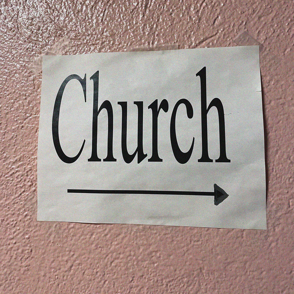 a very DIY printer paper sign points to the right and says CHURCH on a pink wall