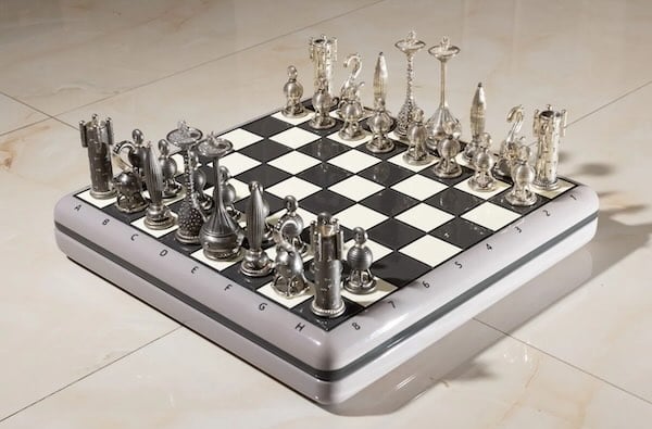 Ajedrez con piezas metálicas y con diamantes. El tablero es de corte retrofuturista y las piezas son de dos tonos plateados distintos, con formas muy inspiradas por lo digital y una estética eslava algo arabizada.