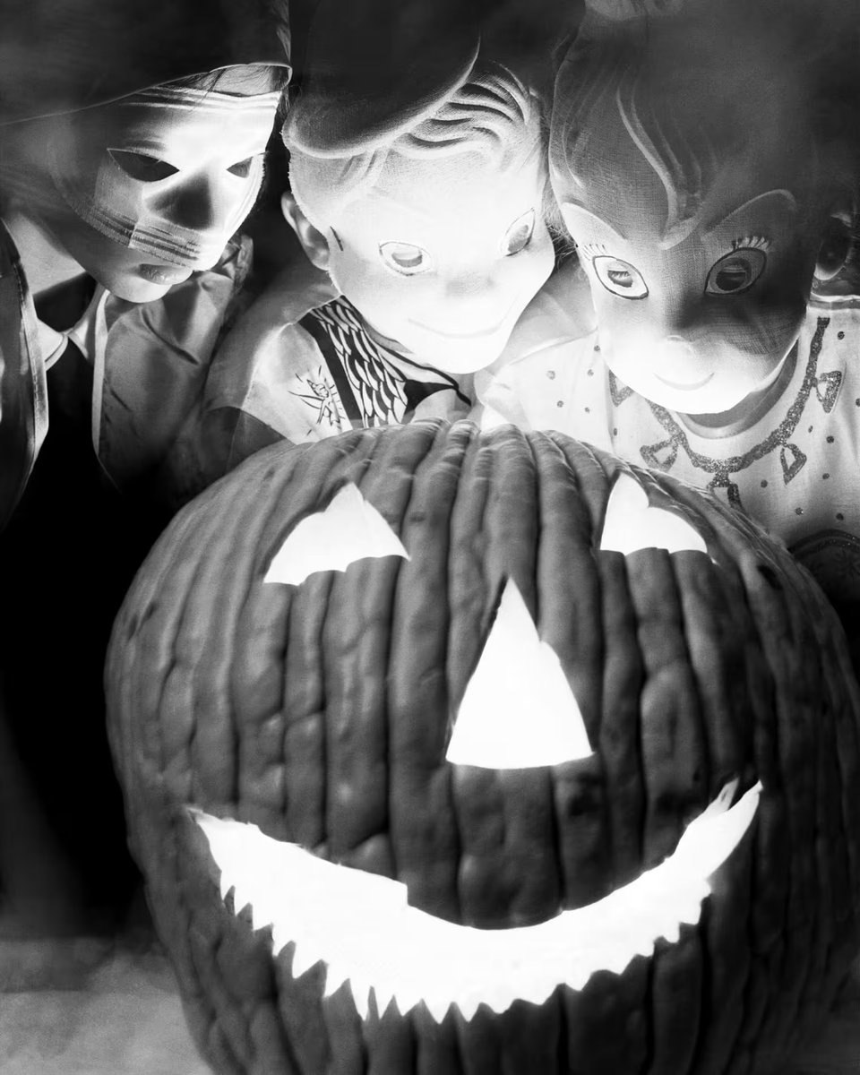 Three children in creepy masks lean over a lit jack o'lantern