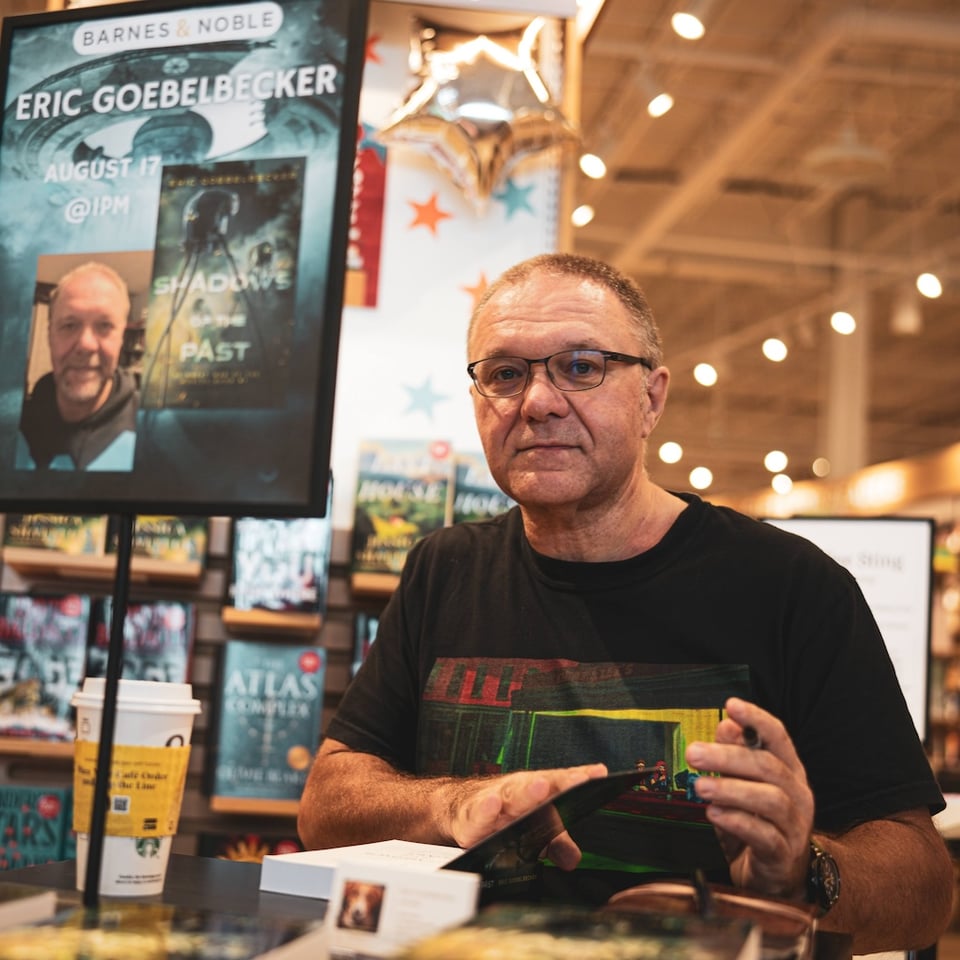 Author sitting at table signing a book.