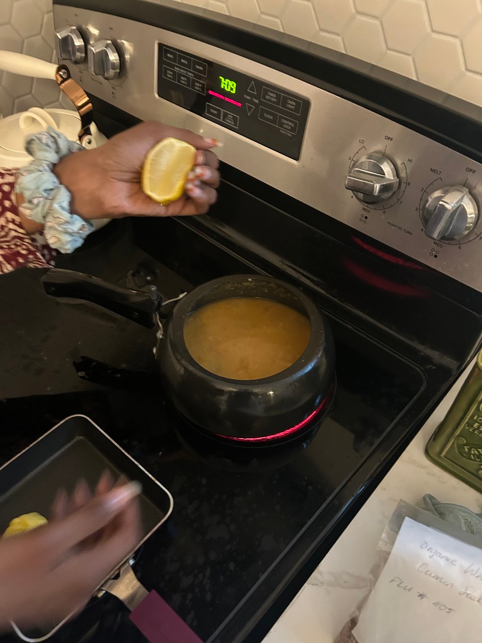 a photograph of an open pressure cooker with lentil soup inside of it and a brown hand squeezing a lemon into the pressure cooker