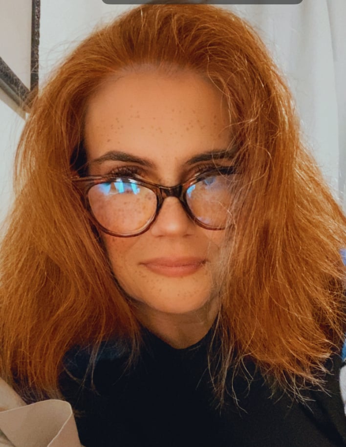 a woman with red hair, cat eye reading glasses, and a faint smile