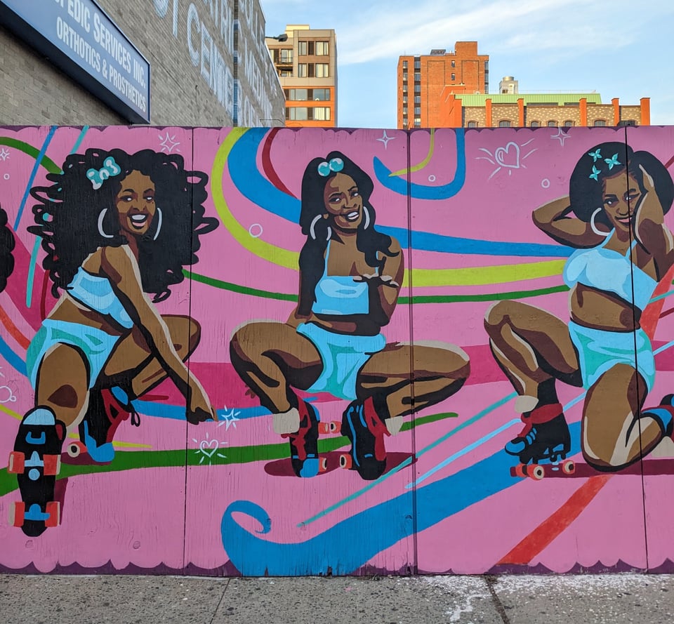 Mural beside a construction site of three Black women in roller skates and turquoise clothing on a pink background