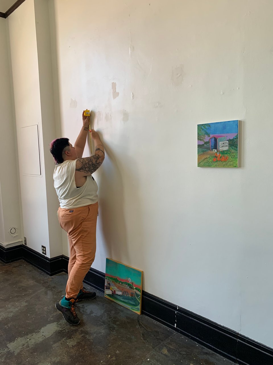 a gender queer person installing paintings on a wall