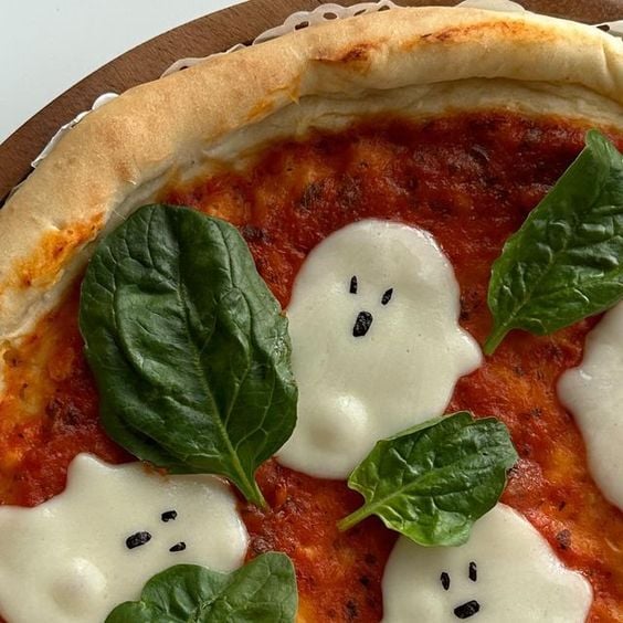 A close-up image of a pizza with ghost-shaped blobs of mozzarella and regular-shaped basil leaves