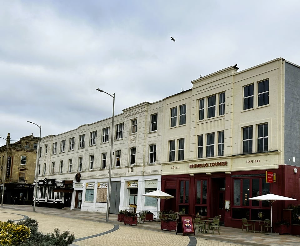 A photo of the Grand Central building today. It has three storeys. The ground floor contains several sperate shops, one of which is boarded up, and the upper floors are sash windows. There is nothing to indicate its past.
