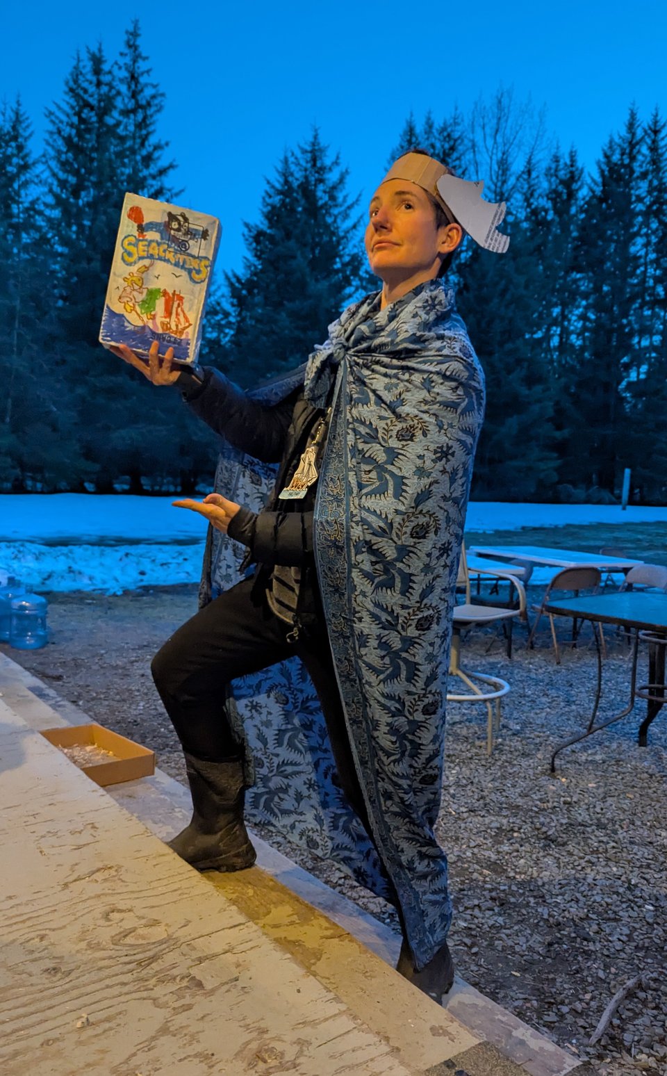 Lucy wearing a tablecloth cape and a cardboard headdress looking noble and holding up a janky cardboard book facsimile.