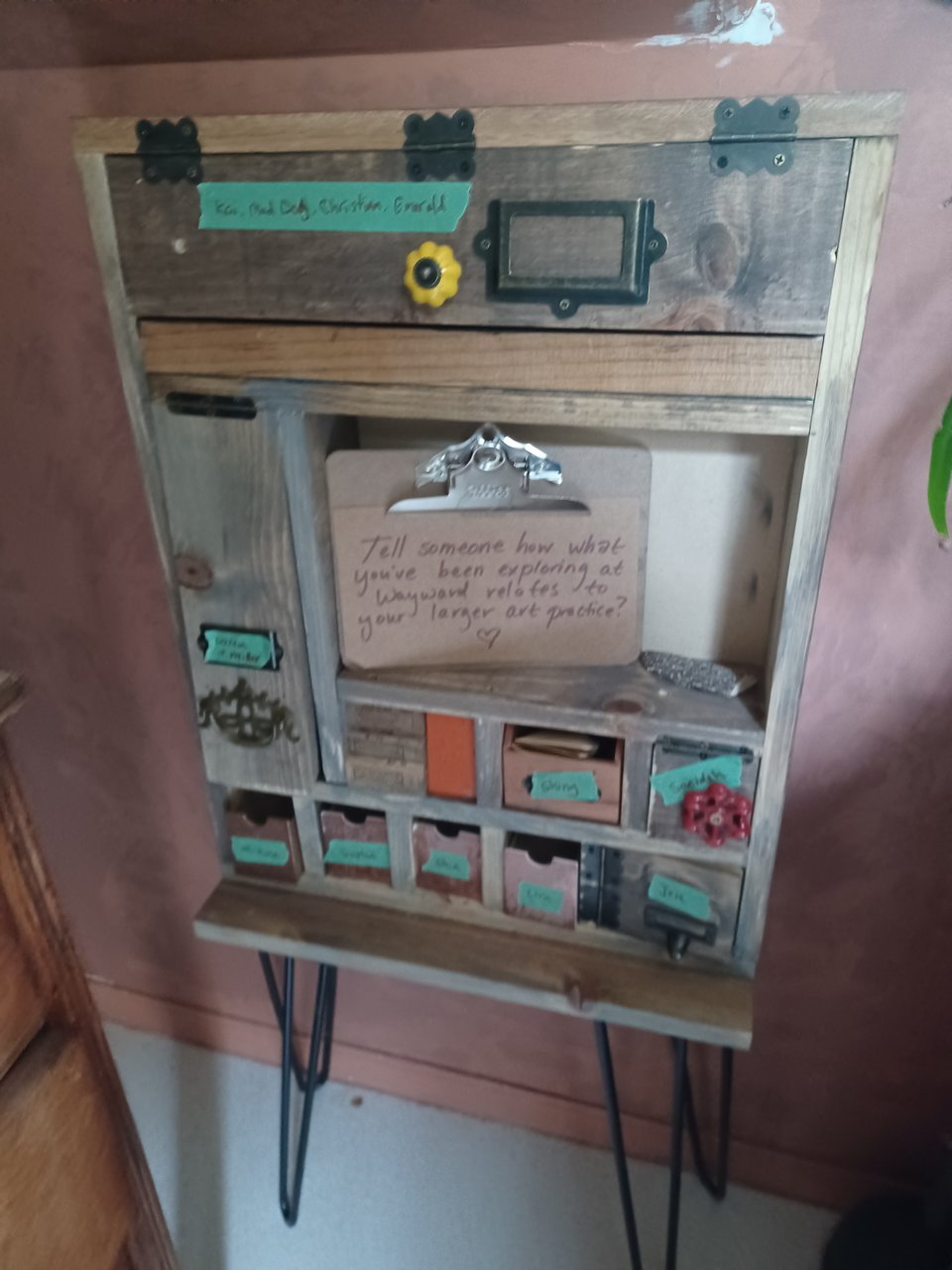 vertical wooden cabinet with many small drawers labeled with names written on painter's tape