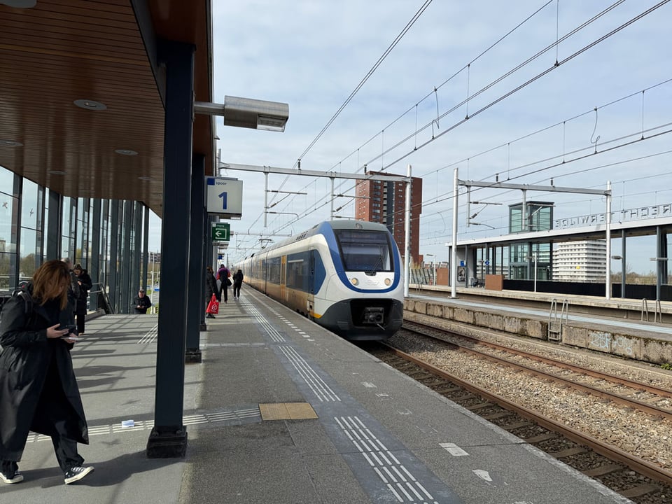 A train approaches a platform as people await to board.