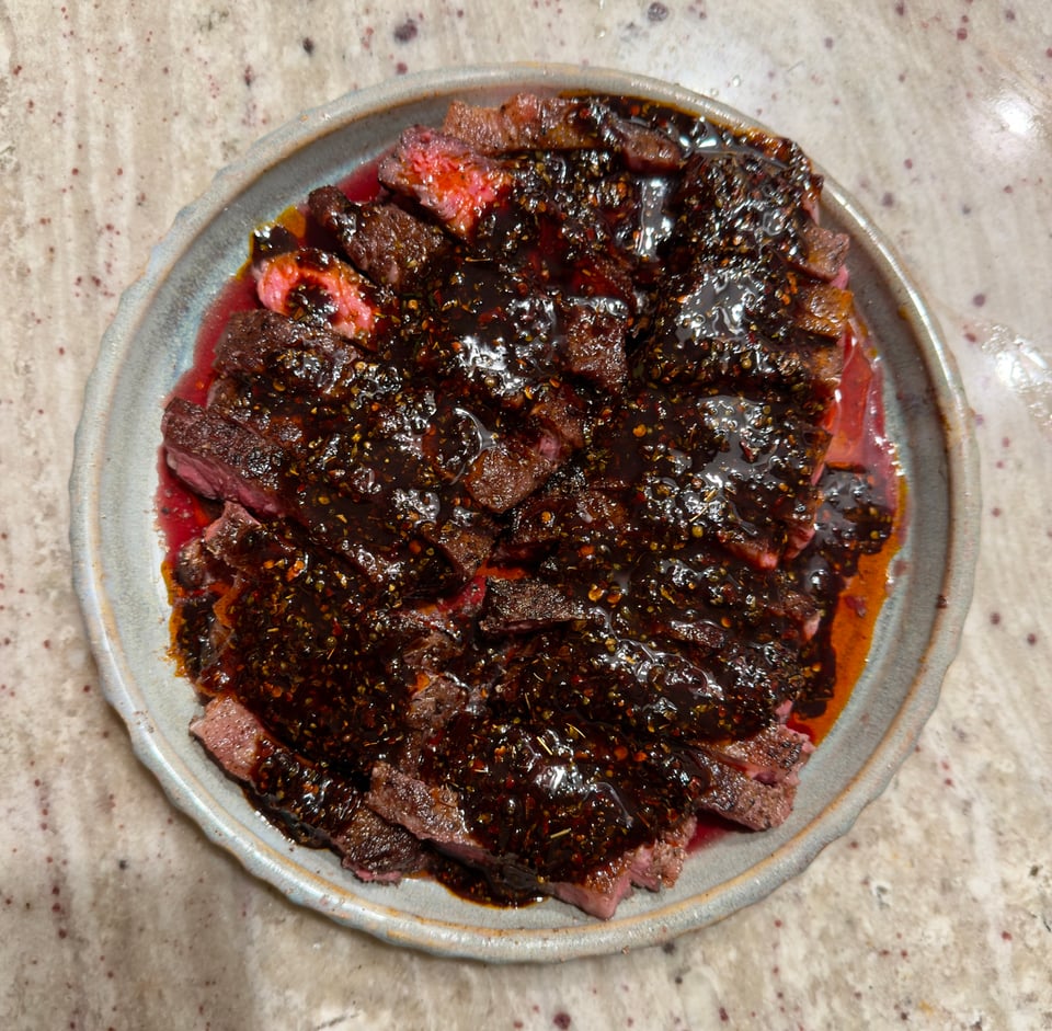 A large portion of strip steak spread on a plate and essentially smothered with a dark red chimichurri sauce.