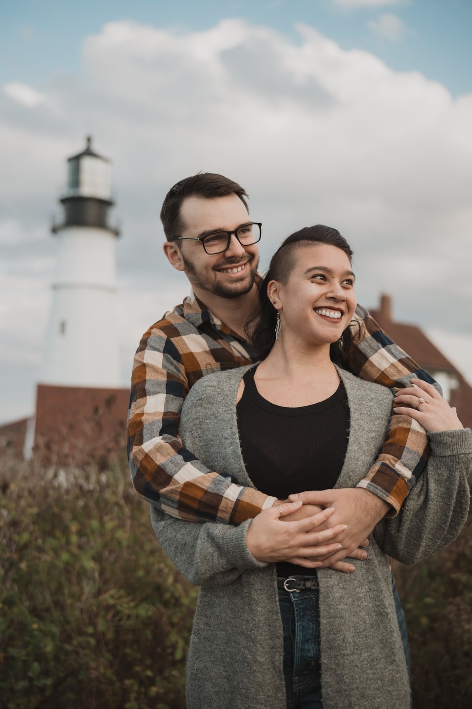 a couple hugging in front of a lighthouse